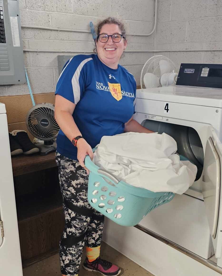 Laundry Employee, Emily, smiling as she loads white sheets into a dryer.