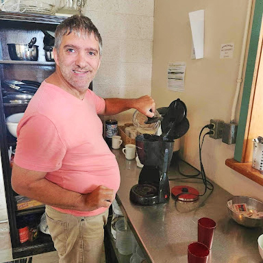 Joseph smiles at the camera while preparing a pot of coffee at the Pugwash Social Hub.