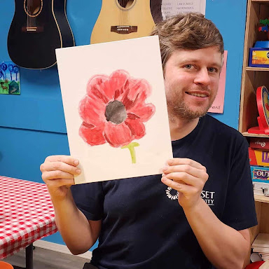 Stephen smiles and holds his painting of a poppy up for the camera.