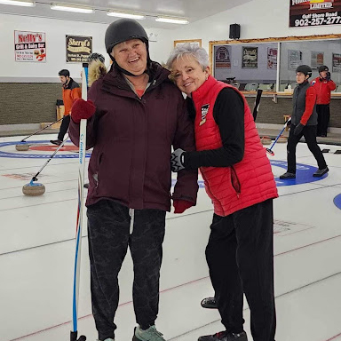 Standing on the ice in a curling rink, a program participant and volunteer embrace and smile, looking at the camera.